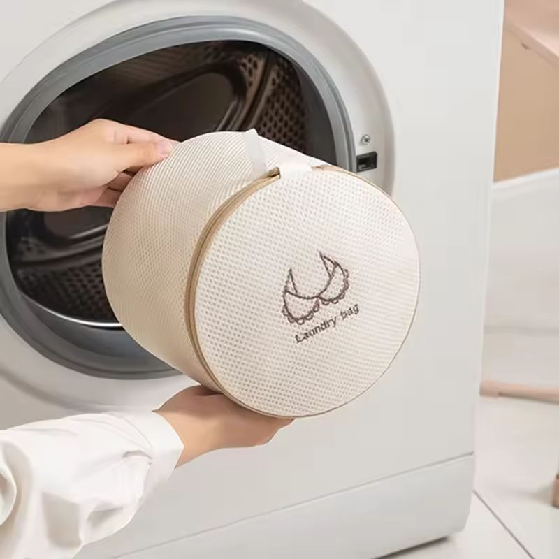 Person holding a round laundry bag in front of a washing machine